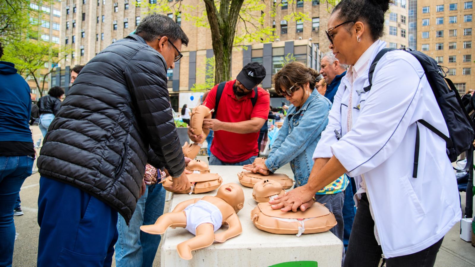 Community members practice CPR techniques on training mannequins during an outdoor Community Ready event at CUIMC.