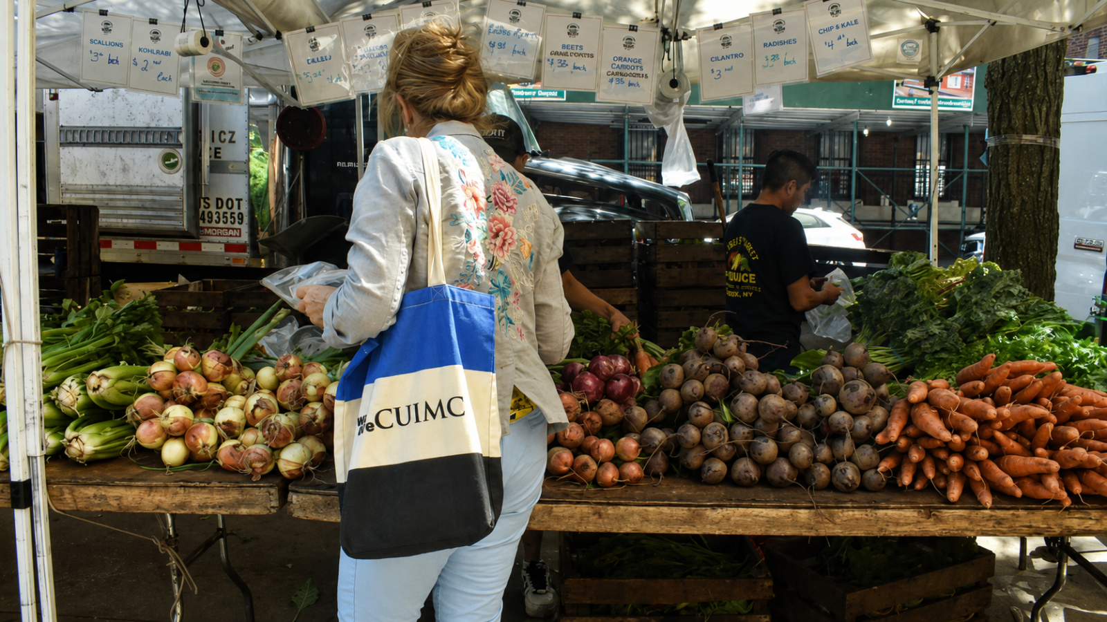 A shopper carrying a CUIMC tote bag selects fresh vegetables at the Greenmarket in Haven Plaza.