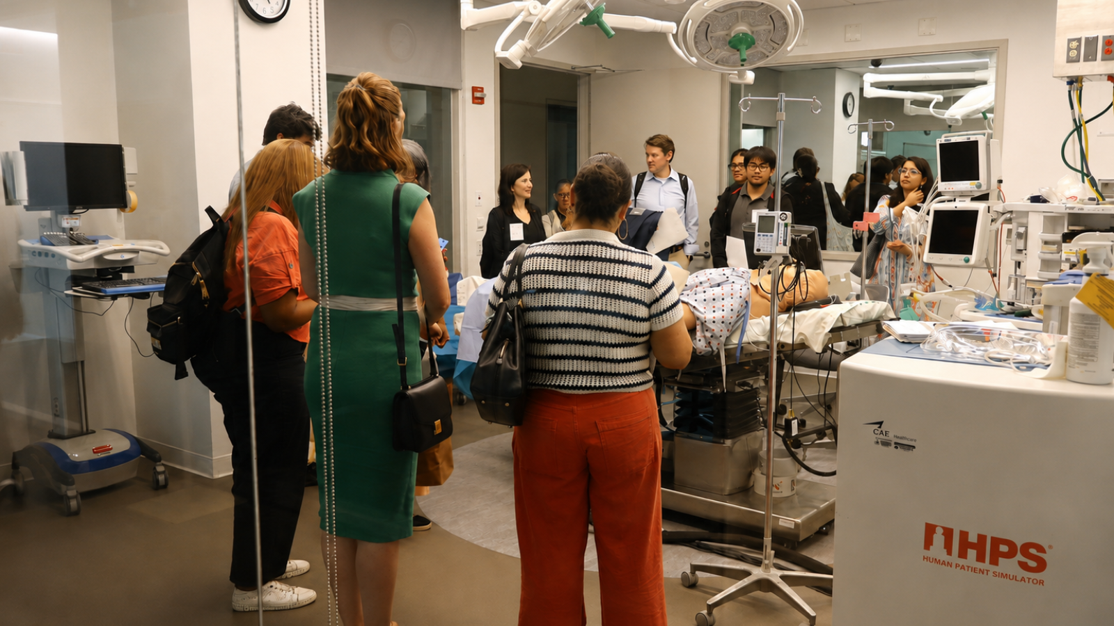 A group of visitors gathers around a medical simulation mannequin and clinical equipment during a hands-on demonstration in a simulation lab.