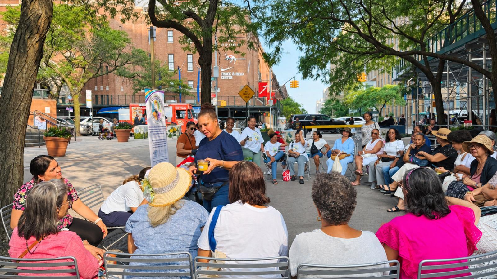 Participants sit in a circle beneath the trees at Haven Plaza as a woman speaks to the group during a S.A.B.O.R. Muévete event.